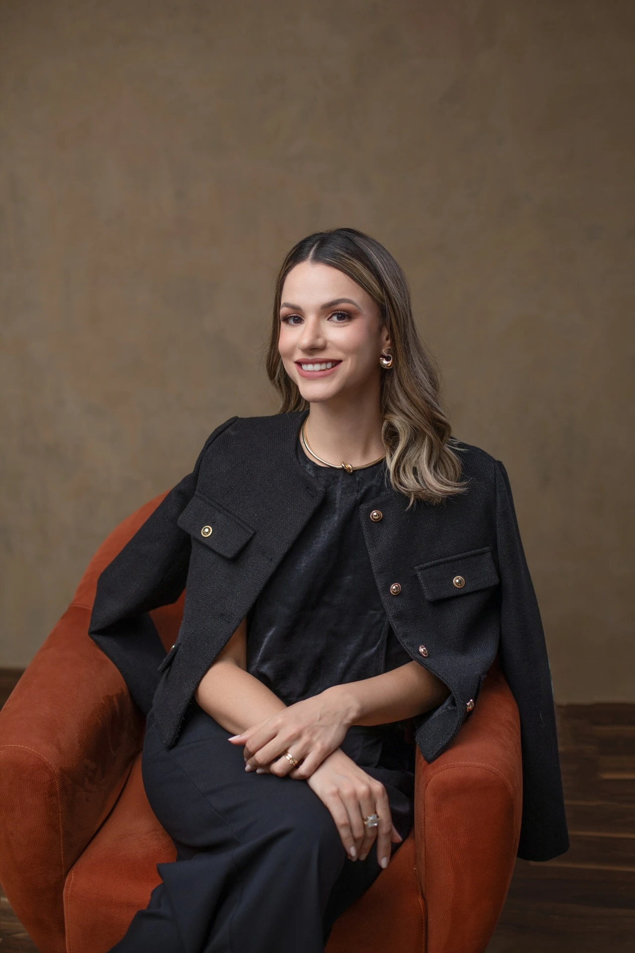 Dra. Letícia Loureiro, sorrindo, com roupa preta, sentada em uma poltrona